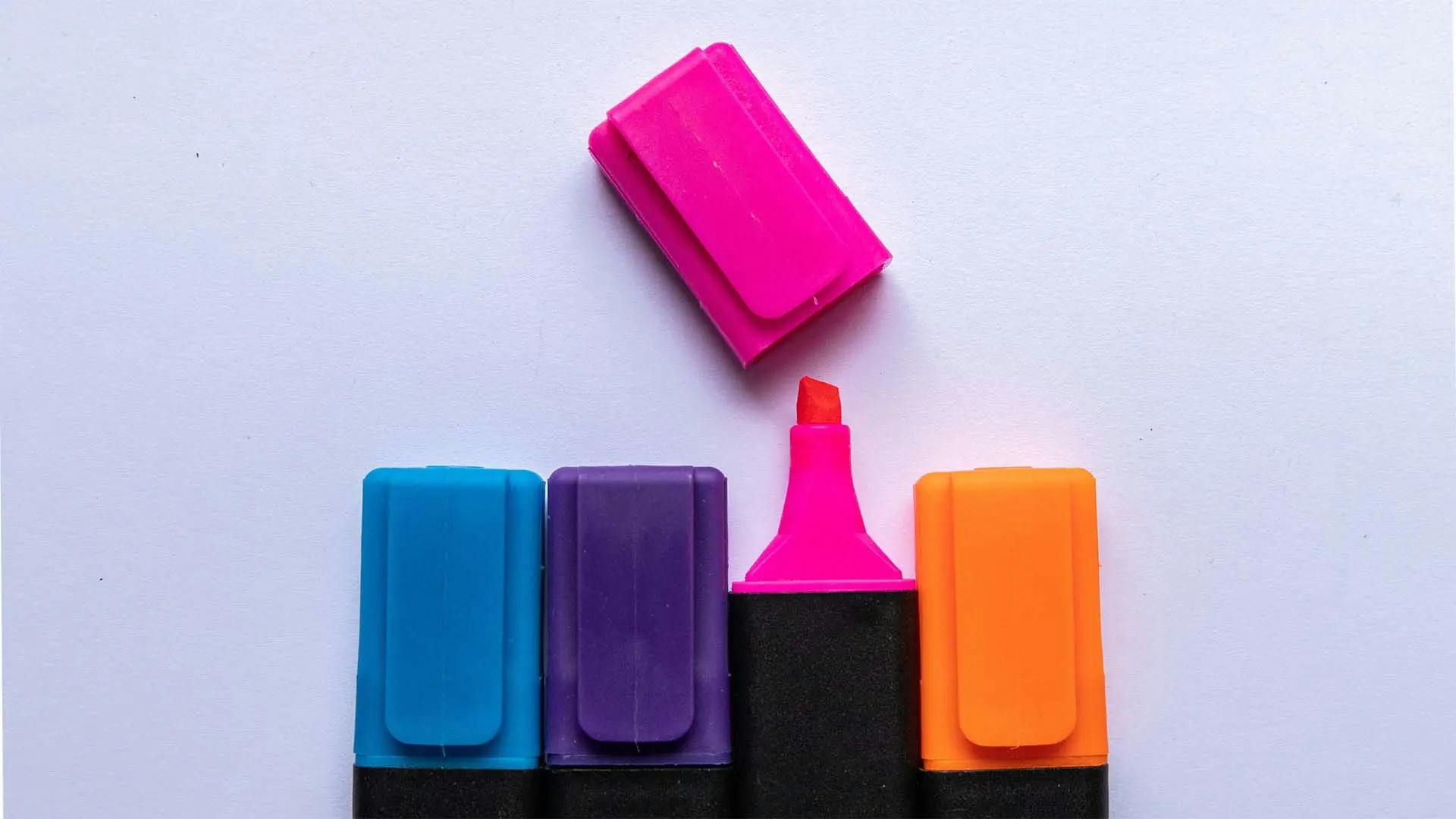 Four highlighter pens in various colors, and the pink highlighter has its cap removed