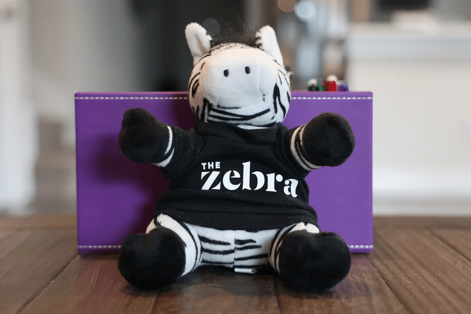 A stuffed Zebra wearing a black t-shirt with The Zebra logo on it