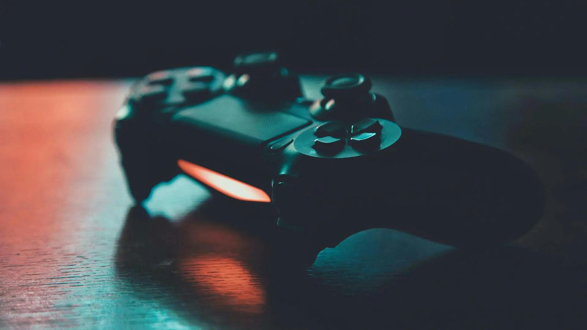 A gloomy photo of a PlayStation 4 controller with strong shadows and subtle orange and green lighting
